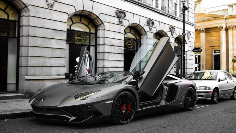 Grey matte Lamborghini Aventador SV Roadster with both doors open is parked